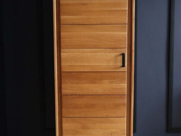 Wąska szafa dębowa z pojedynczymi drzwiami, czarny uchwyt, osadzona na tle granatu