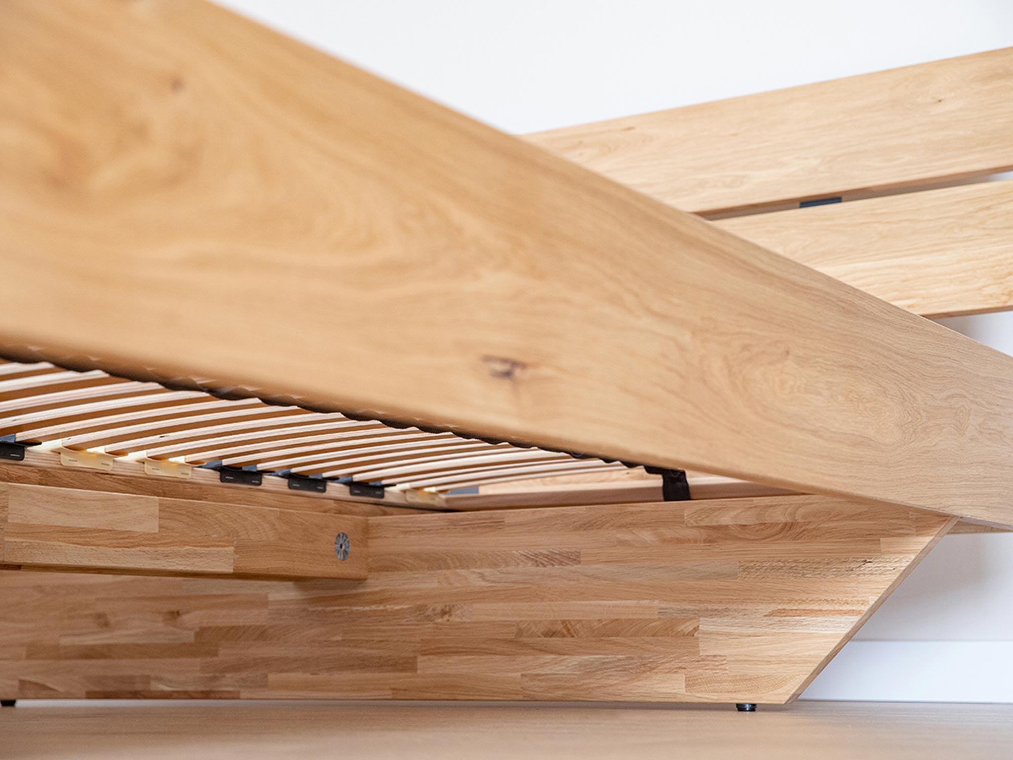 Zbliżenie na narożnik łóżka z czarnym wspornikiem i drewnianą ramą w stylu technicznym