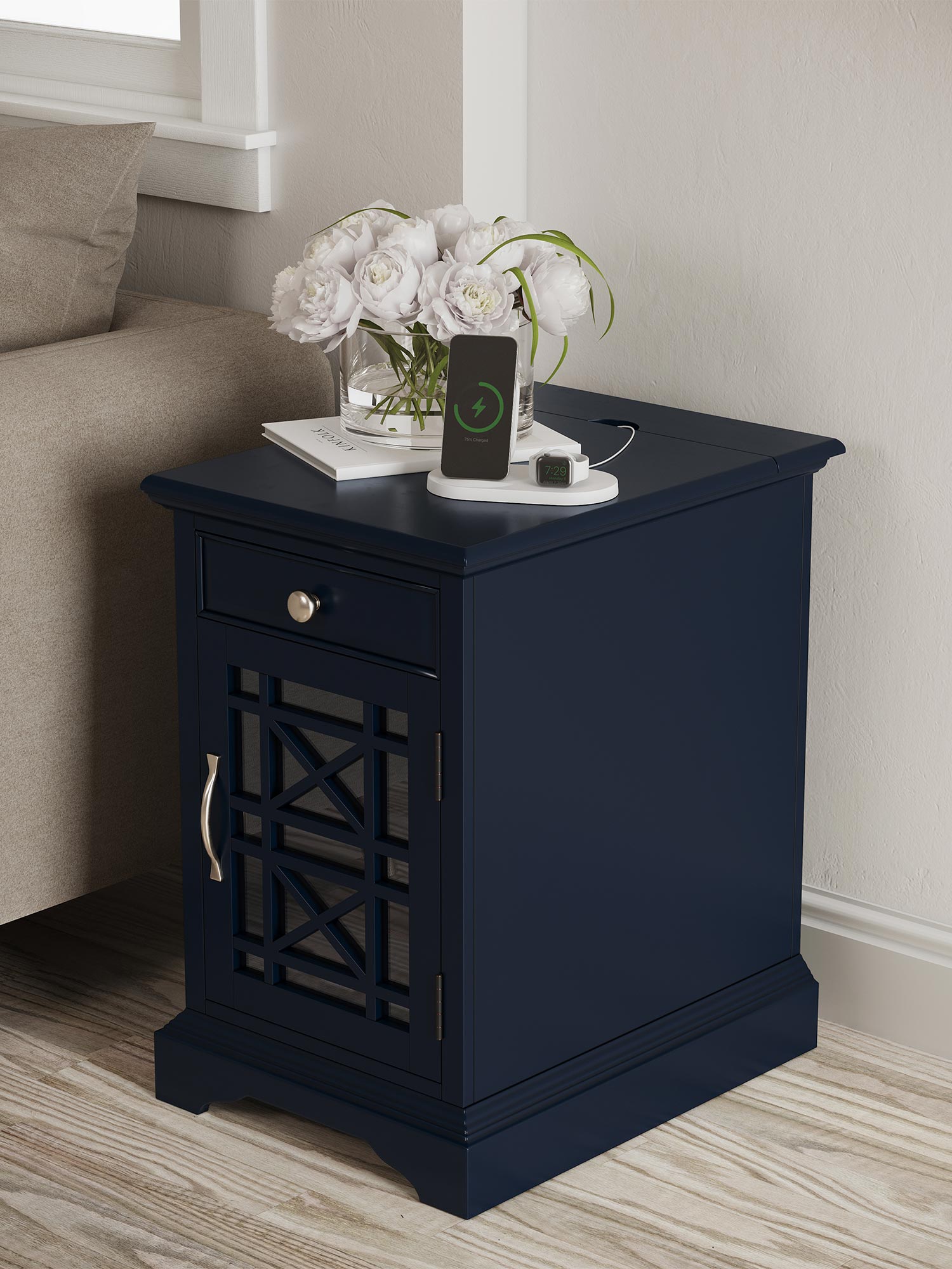 Granatowa szafka nocna z pojedynczą szufladą i srebrnym uchwytem, ustawiona przy sofie z dekoracją kwiatową Granatowa szafka nocna z pojedynczą szufladą i srebrnym uchwytem, ustawiona przy sofie z dekoracją kwiatową