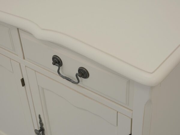 Zbliżenie na bok białej komody z frezowanym frontem i metalowym uchwytem