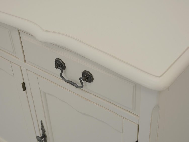 Zbliżenie na bok białej komody z frezowanym frontem i metalowym uchwytem