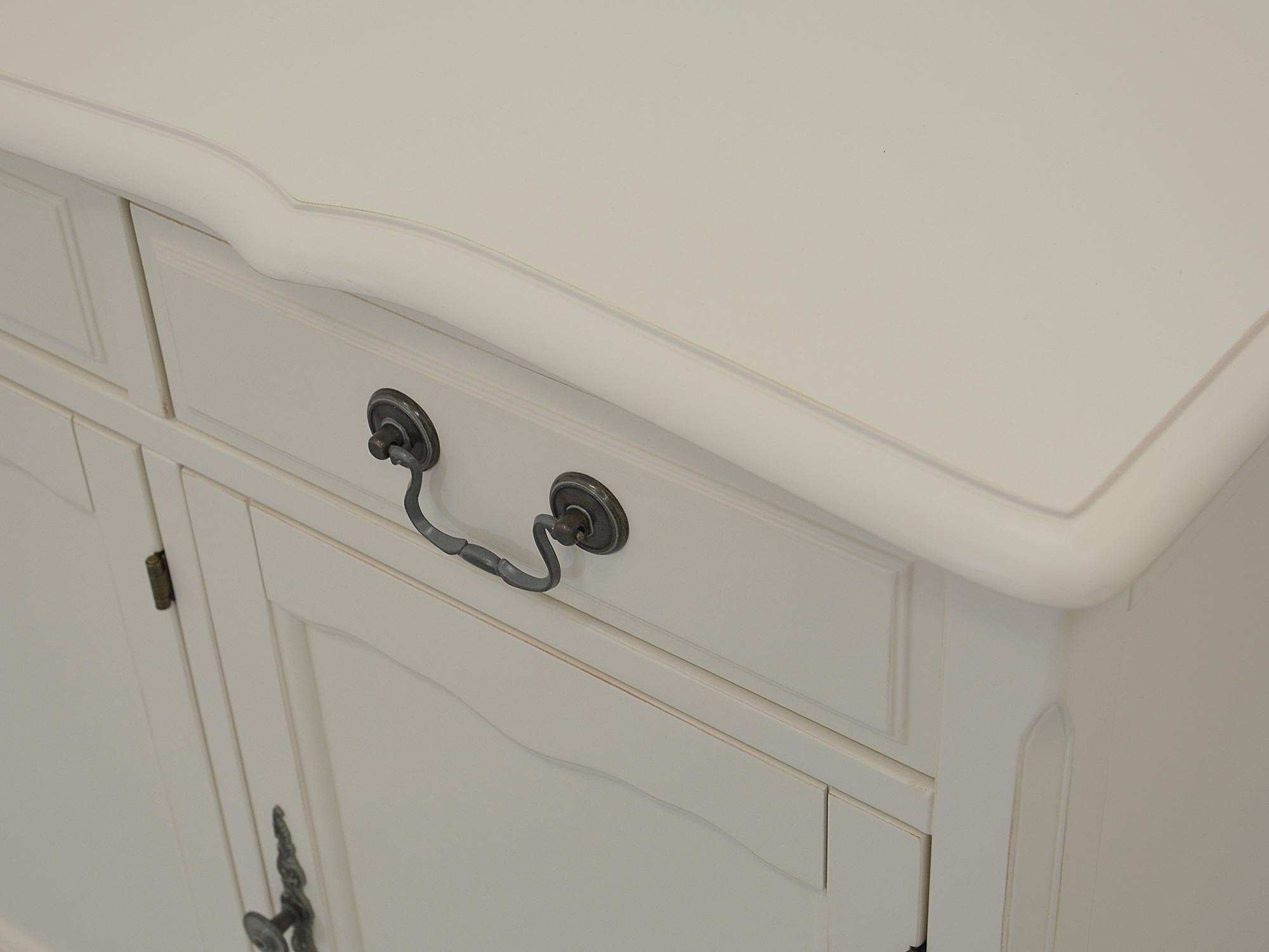 Zbliżenie na bok białej komody z frezowanym frontem i metalowym uchwytem Zbliżenie na bok białej komody z frezowanym frontem i metalowym uchwytem