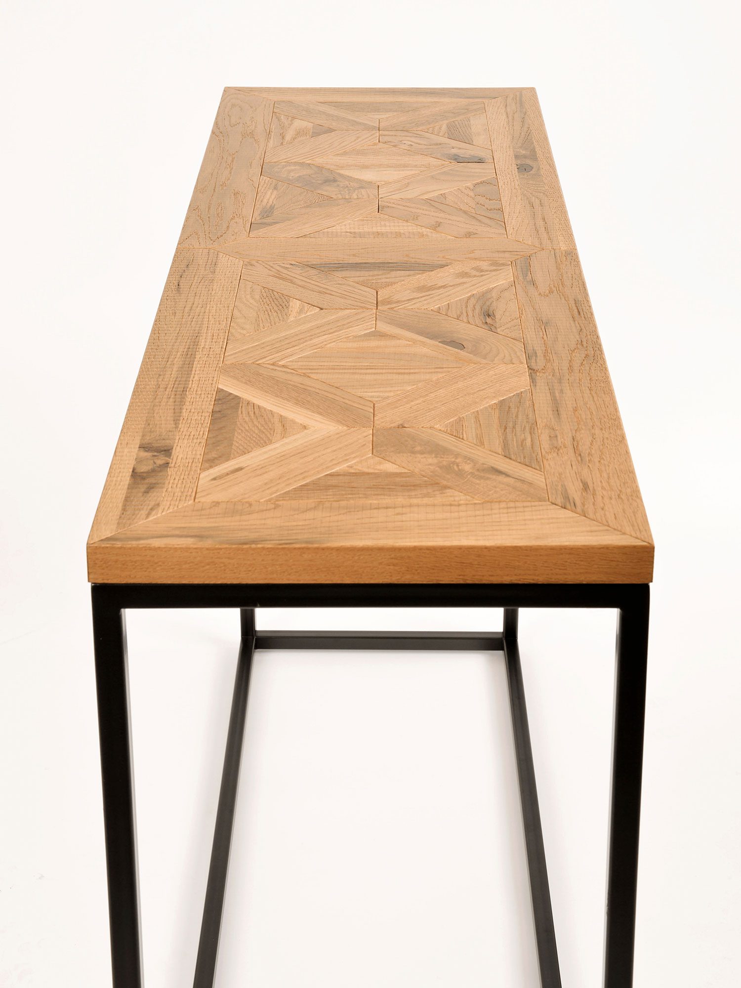 Wąski stolik konsolowy z blatem w jodełkę i czarną metalową ramą, widok z przodu Wąski stolik konsolowy z blatem w jodełkę i czarną metalową ramą, widok z przodu