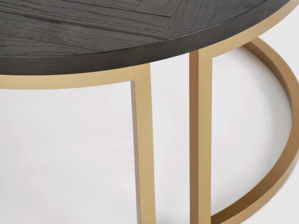 Zbliżenie na stolik kawowy okrągły czarny z blatem w jodełkę i złotą ramą